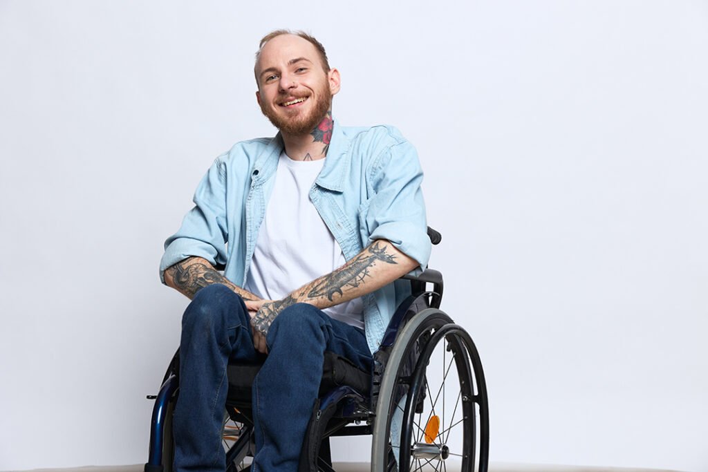 Smiling man with tattoos seated in a wheelchair, representing mobility and independence